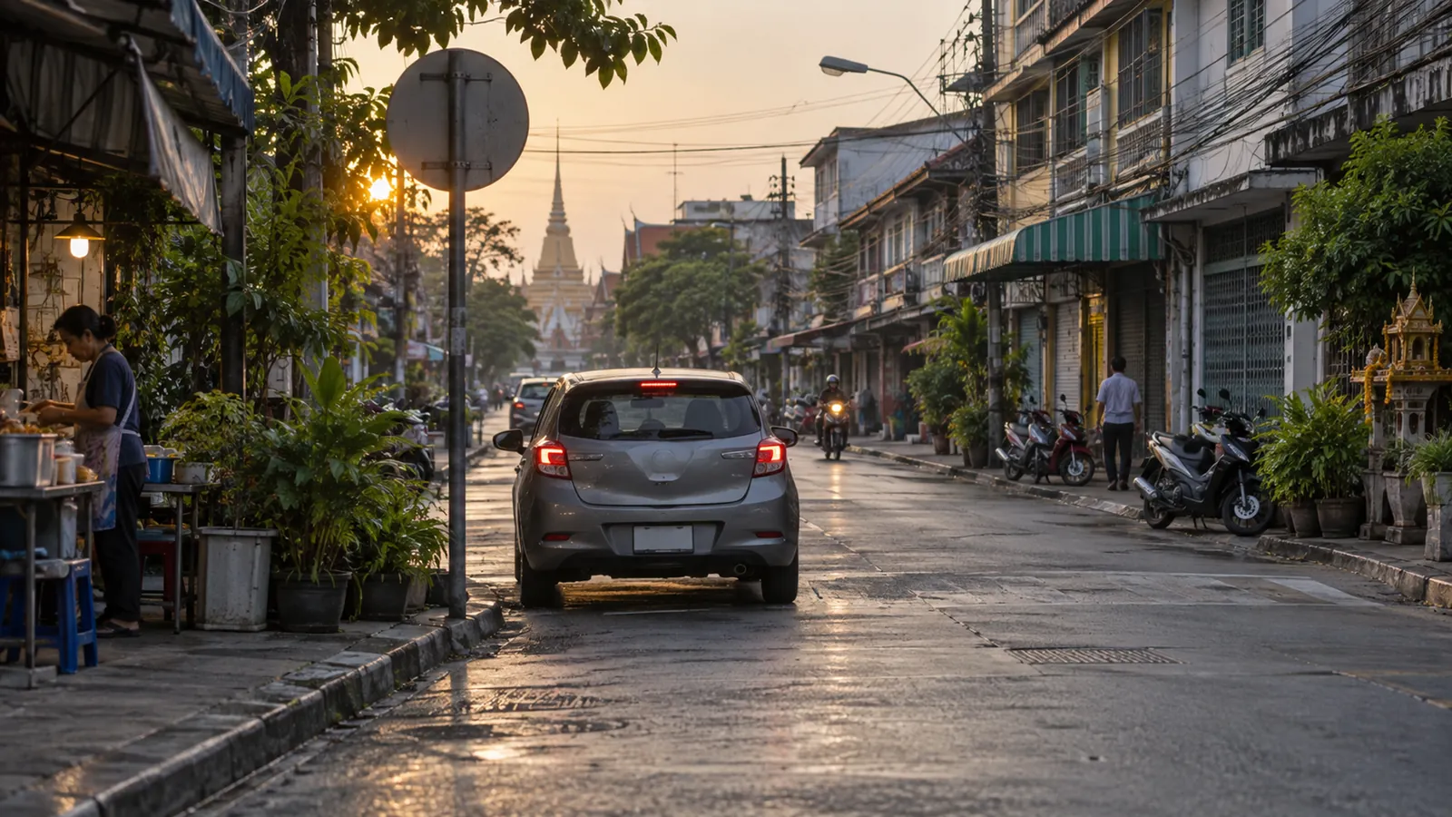 A car heads down a quiet shophouse street at sunrise past a blank round road sign, a temple spire at the far end