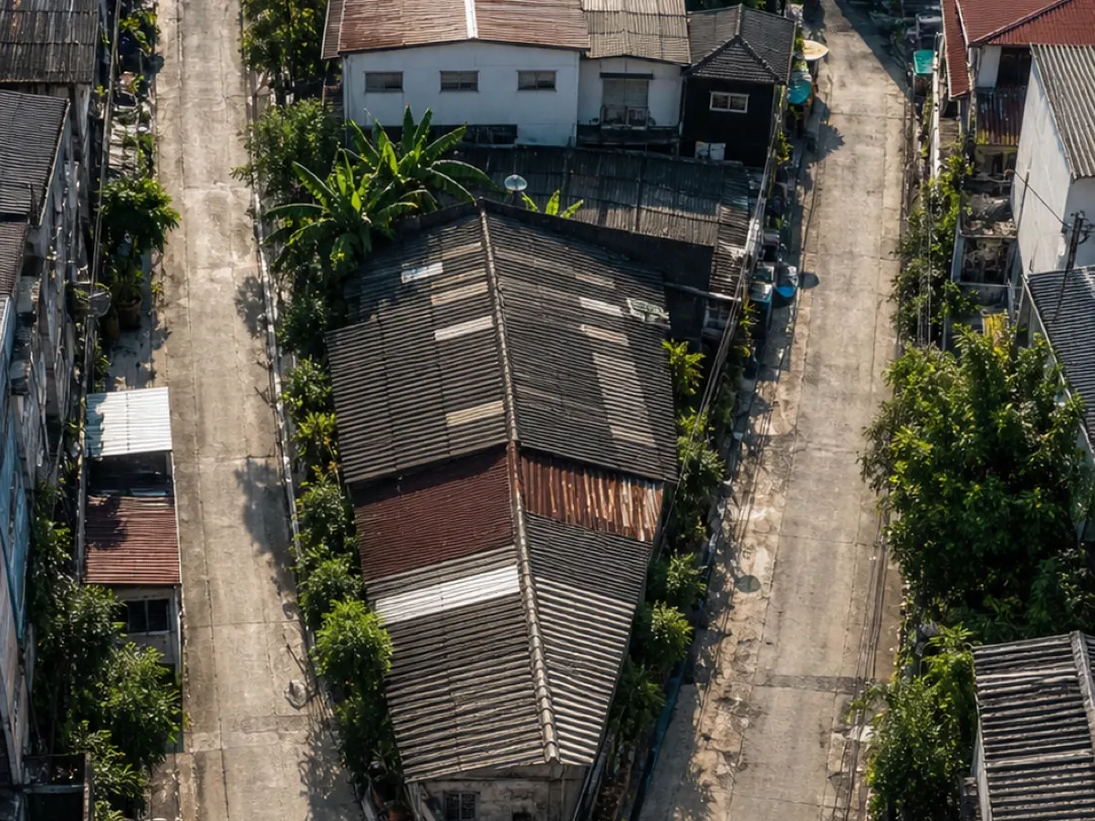 Seen from above, a narrow lane threads between older houses in a tight Bangkok neighbourhood
